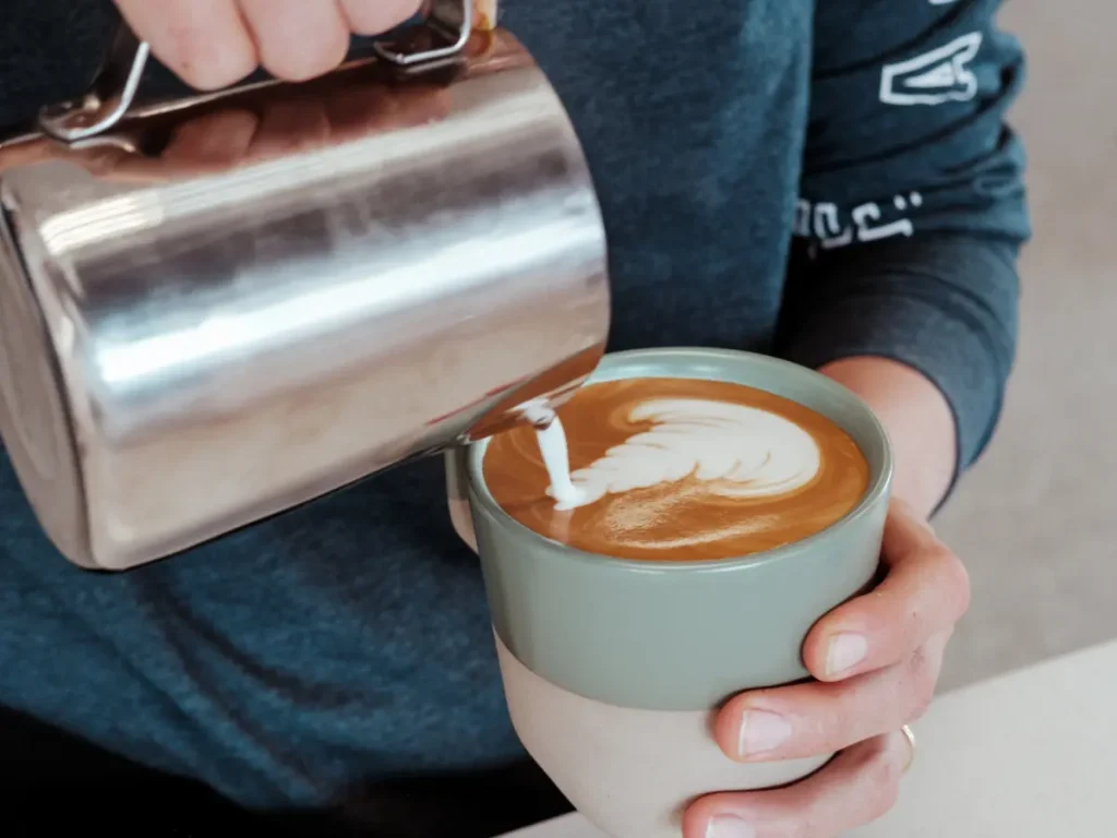 Barista pouring milk into a latin coffee to create latte art at Cafecito